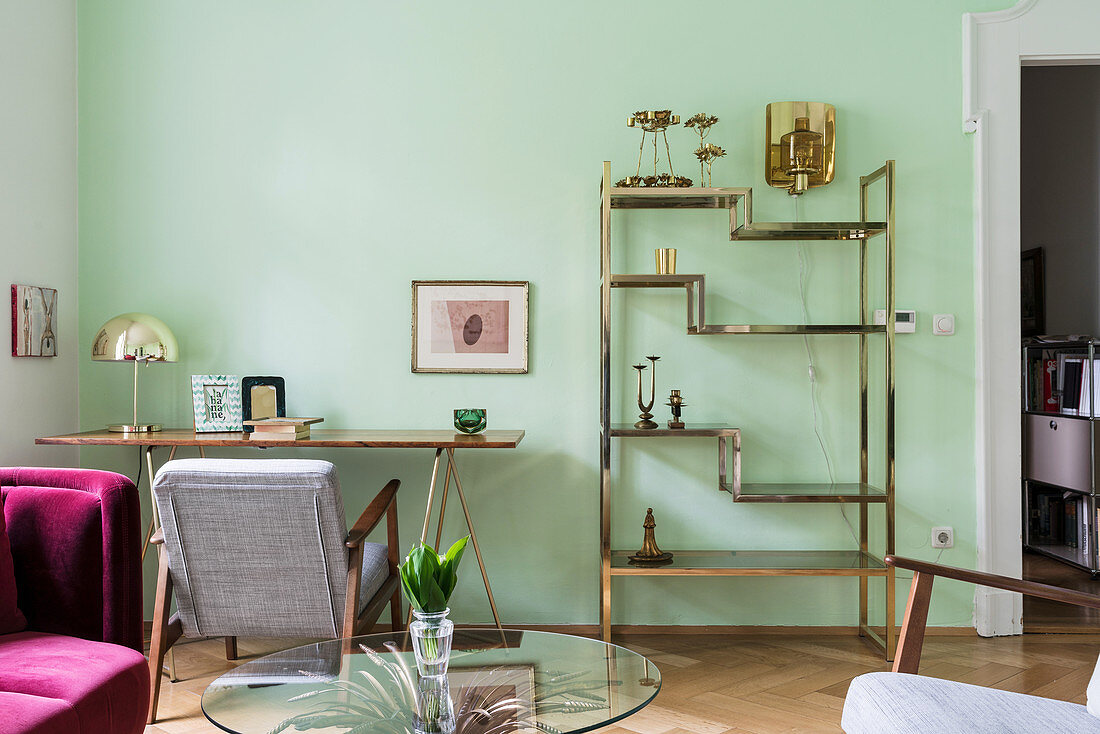 Messing-Regal und filigraner Tisch im Wohnzimmer mit grüner Wand
