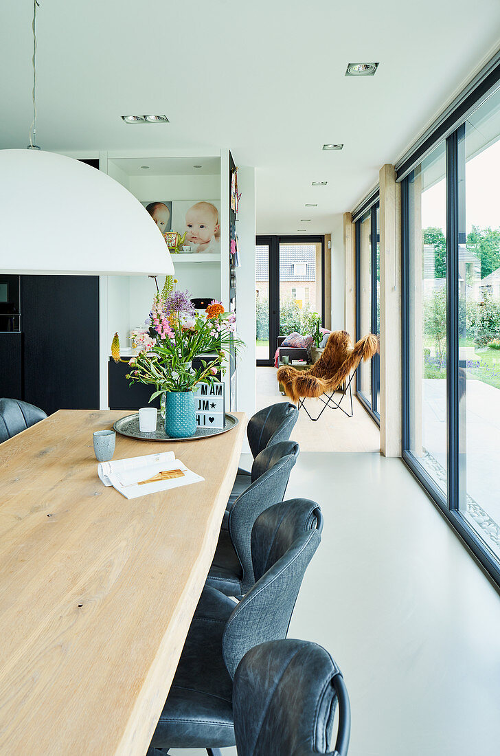Long oak dining table in open-plan interior with glass wall overlooking garden