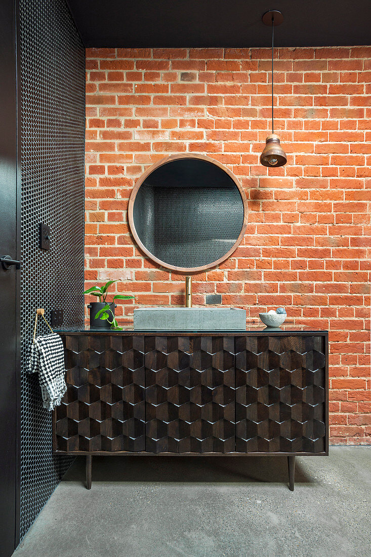 Black vanity with textured front in front of red brick wall in the bathroom