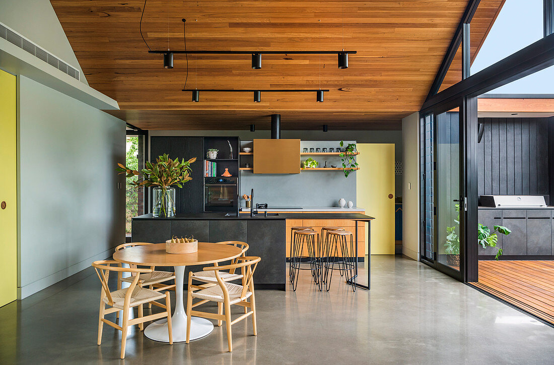 Wohnraum unter Holz-Spitzdach mit offener Küche und raumhohen Schiebetüren zur Terrasse