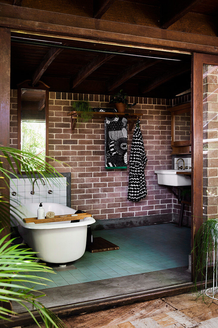 Vintage-Badewanne vor Ziegelsteinwand in naturnahem Badezimmer mit breiter offener Schiebetür