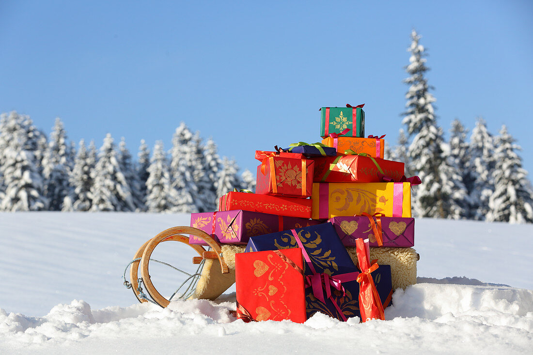 Geschenkpäckchen in farbenfrohem Papier auf Schlitten im Schnee