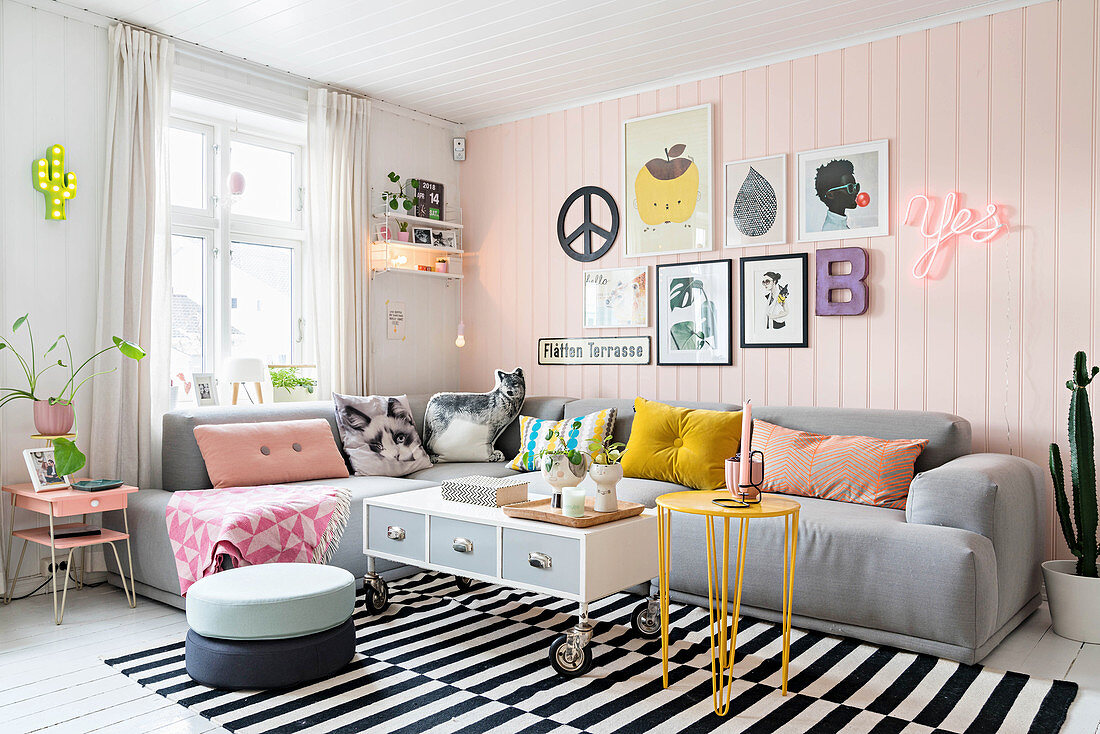 Graues Übereck-Sofa mit dekorativen Kissen in Wohnzimmer mit rosa Holzwand