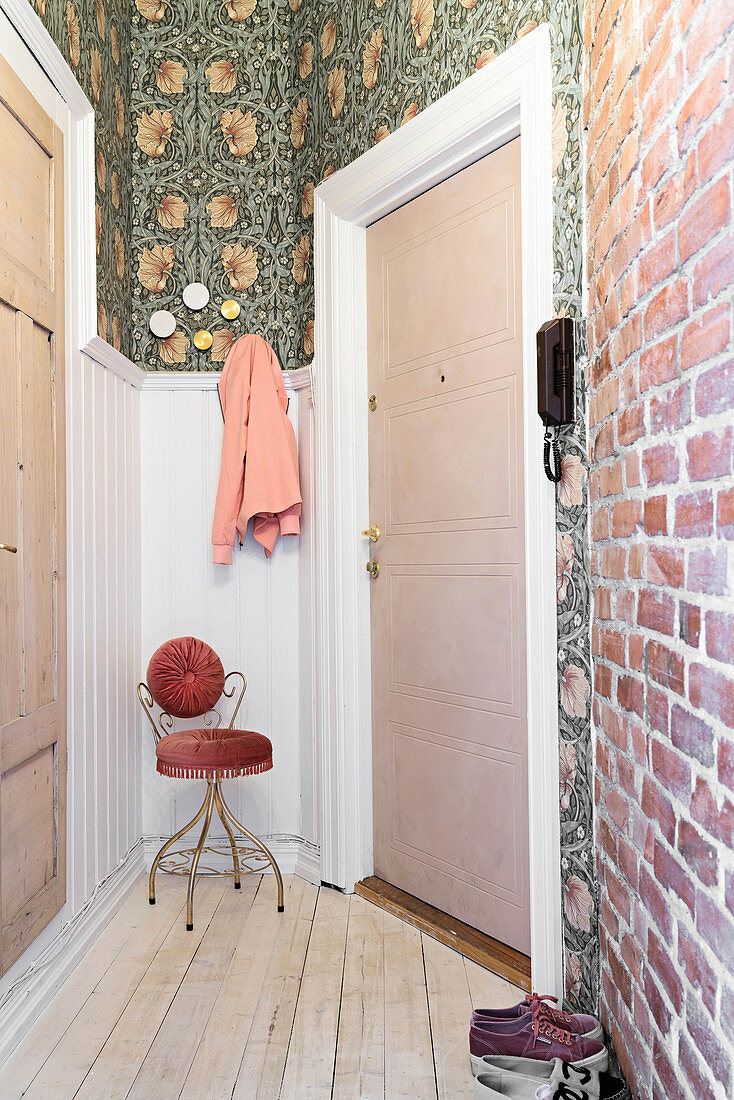 Narrow hallway with brick wall, William Morris wallpaper, wooden doors and antique chair at far end