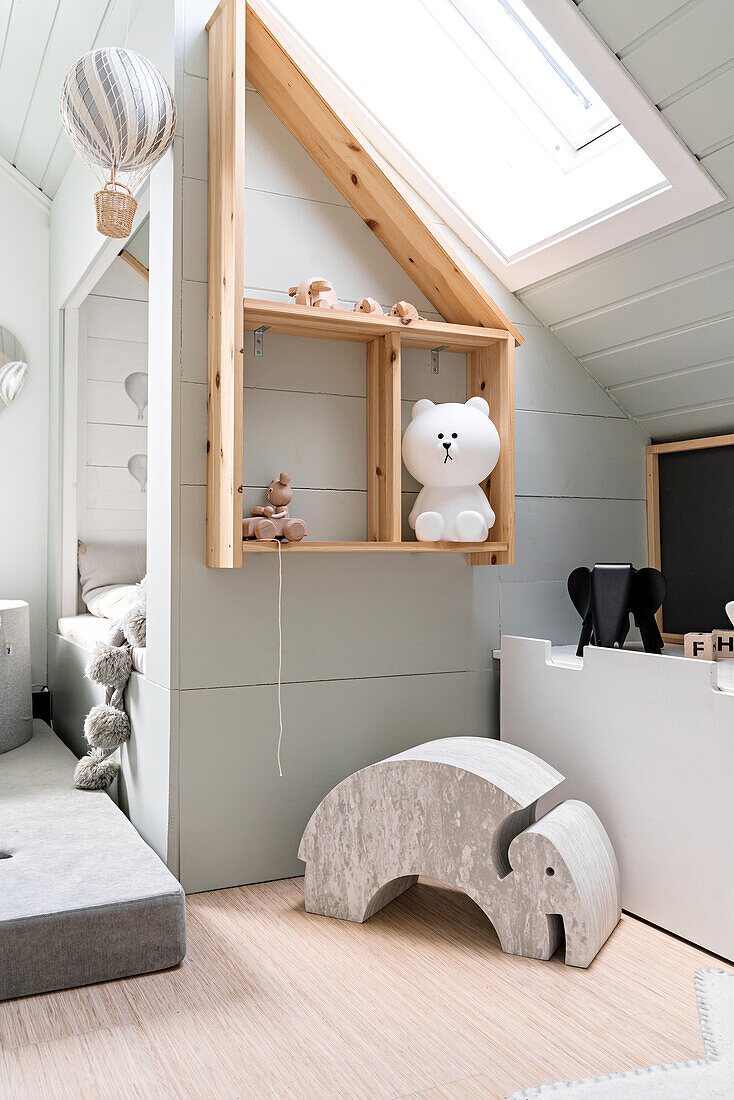 Cubby bed and wooden shelves below sloping ceiling in pale grey child's bedroom