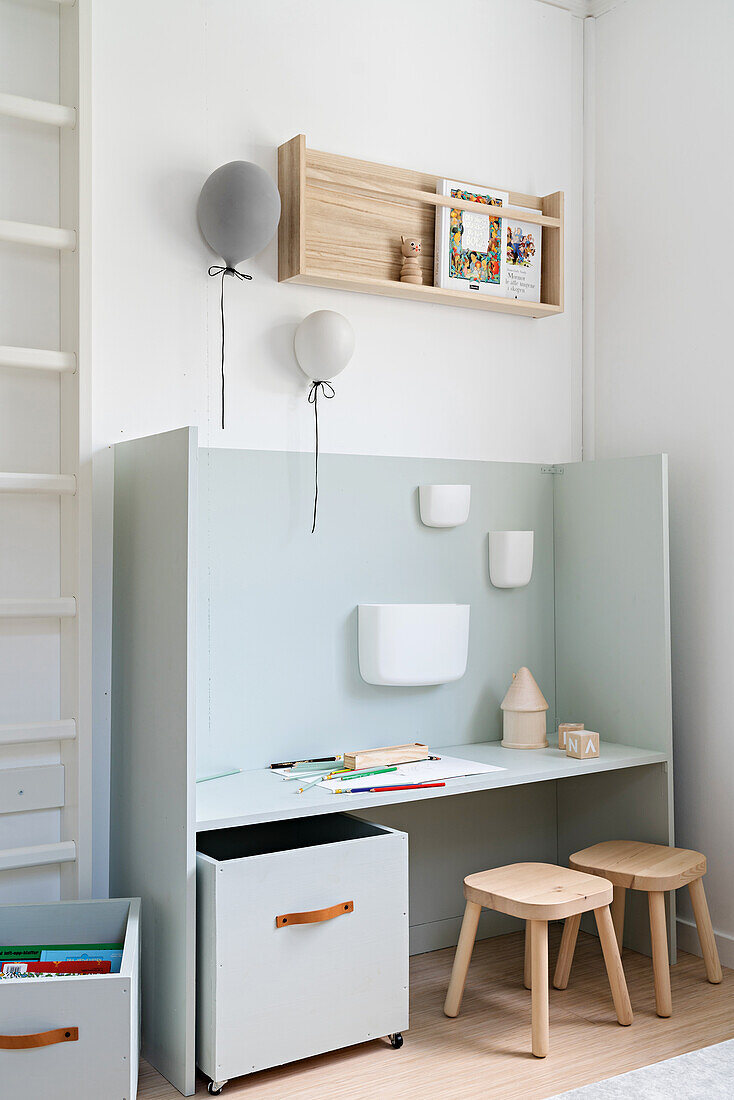 Desk with side walls, container on castors and wooden stools in child's bedroom