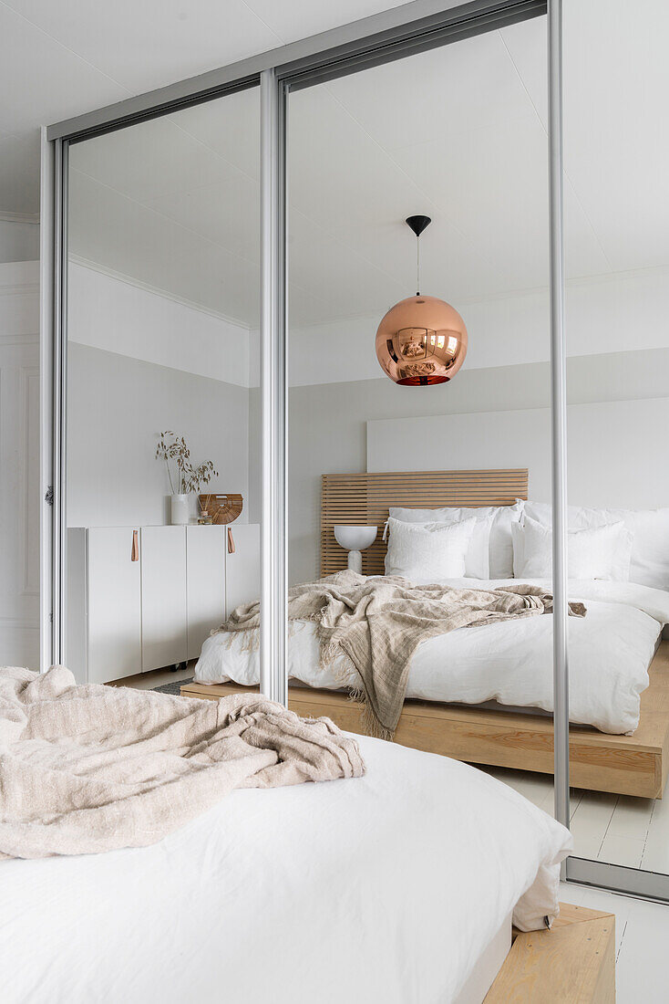 Wooden bed, copper-coloured spherical lamp and floor-to-ceiling mirrored wardrobes in bedroom