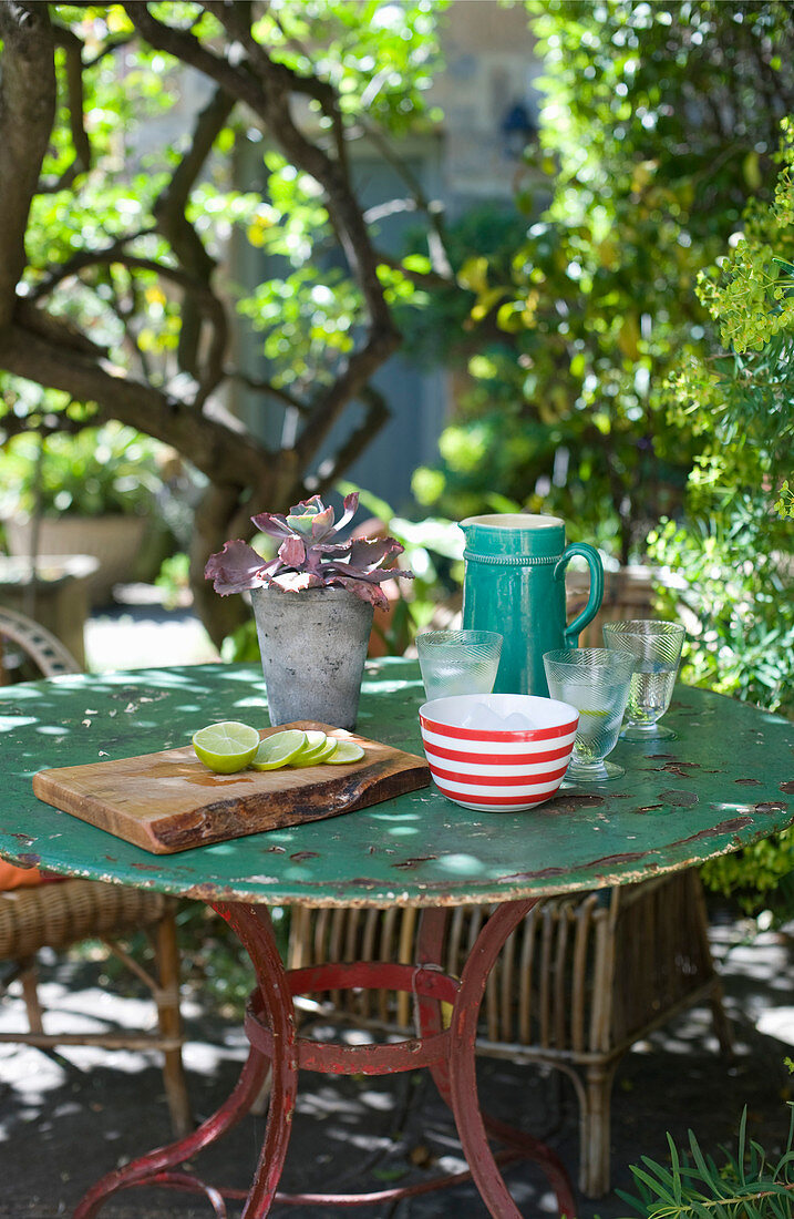 Krug, Gläser und Brett mit Limettenscheiben auf dem Gartentisch
