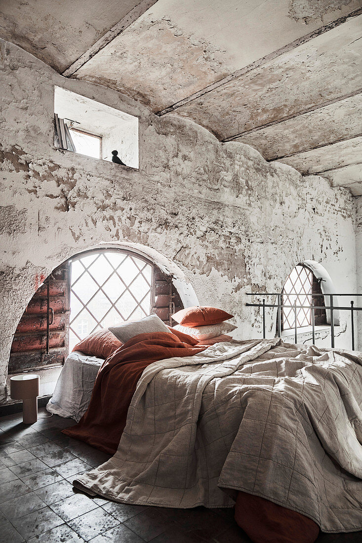 Layered bed linen on bed in old building with vaulted ceiling
