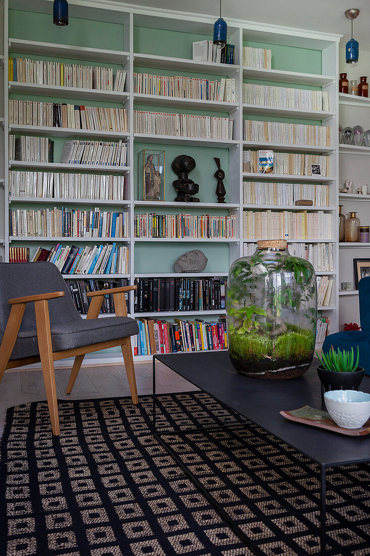 Bottle garden on black coffee table in front of bookcase with mint-green back wall
