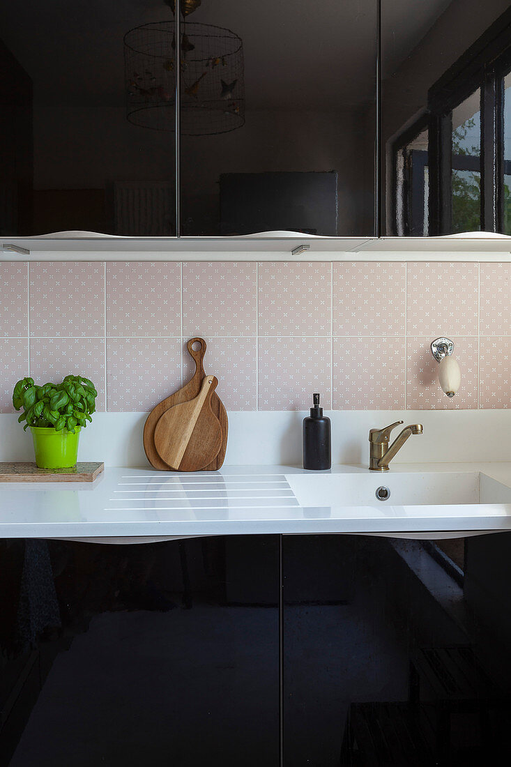 White sink in kitchen with black high-gloss cabinets and pale pink tiled splashback