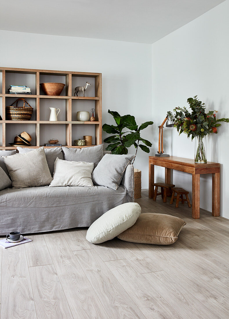 Sofa mit grauer Husse und Kissen vor offenem Holzregal im Wohnzimmer