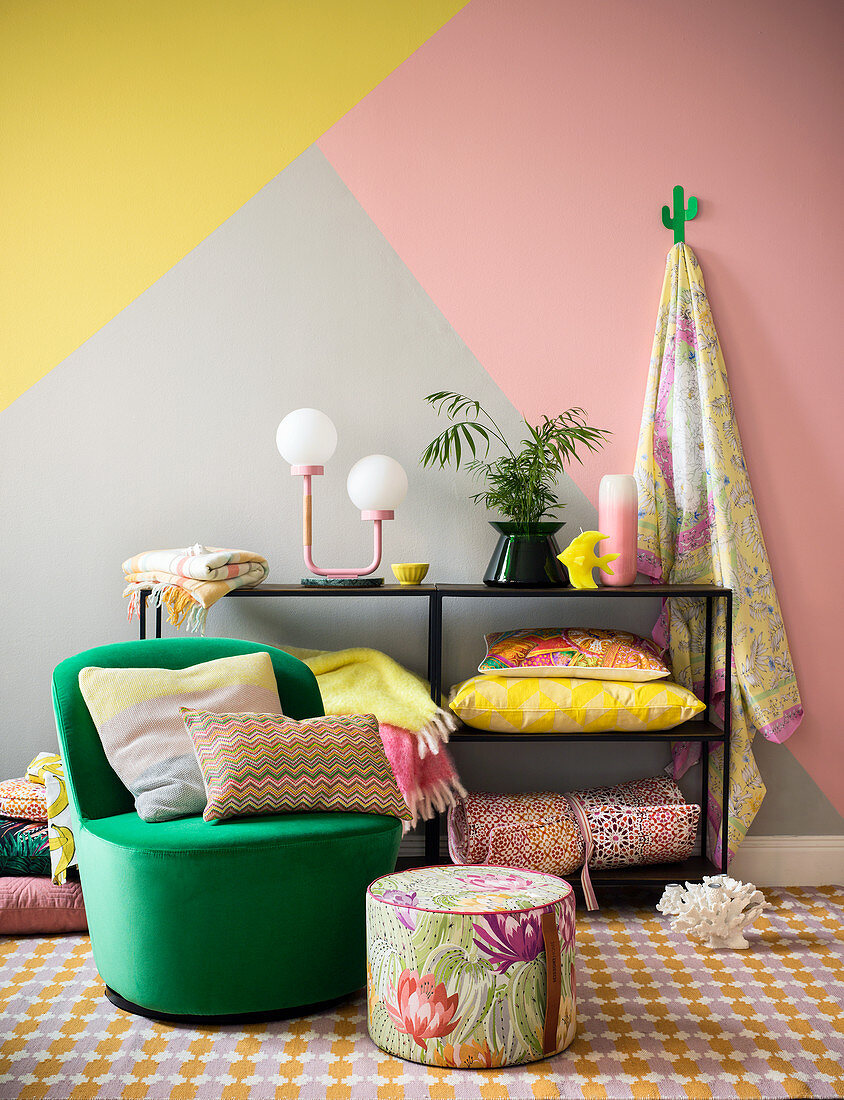 Colourful design: striped cushion on green armchair, floral pouffe and home accessories on shelves against three-tone wall