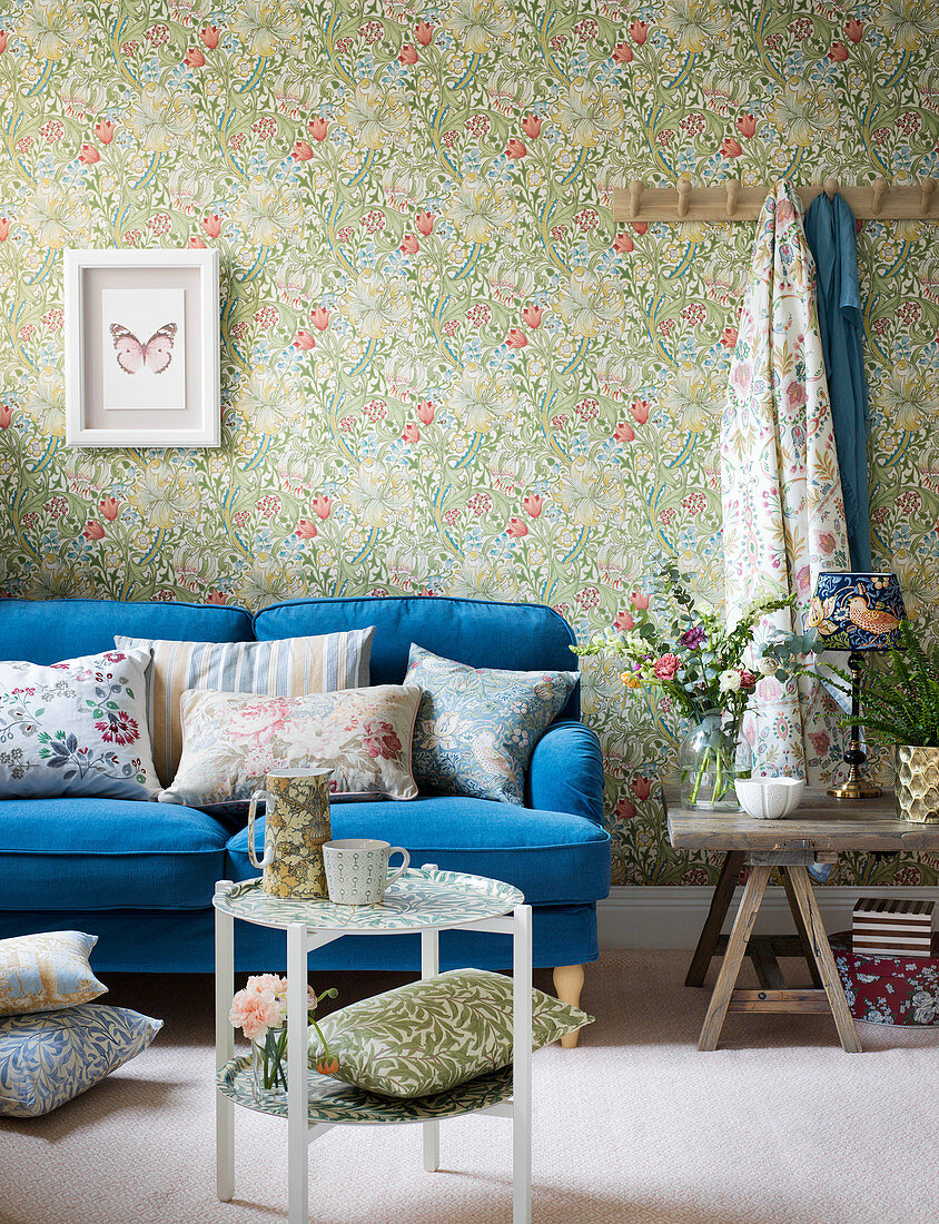 Blumen-Design: Blaues Sofa mit Kissen vor Blumentapete