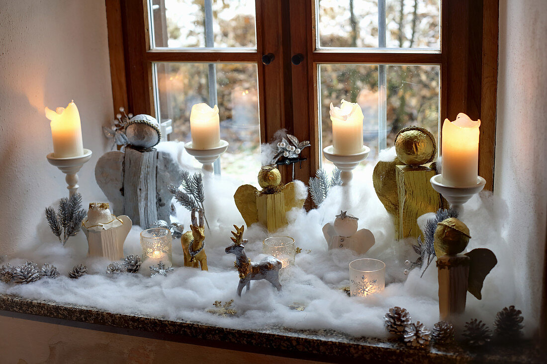 Handmade Christmas angels and candles surrounded by cotton-wool snow on windowsill