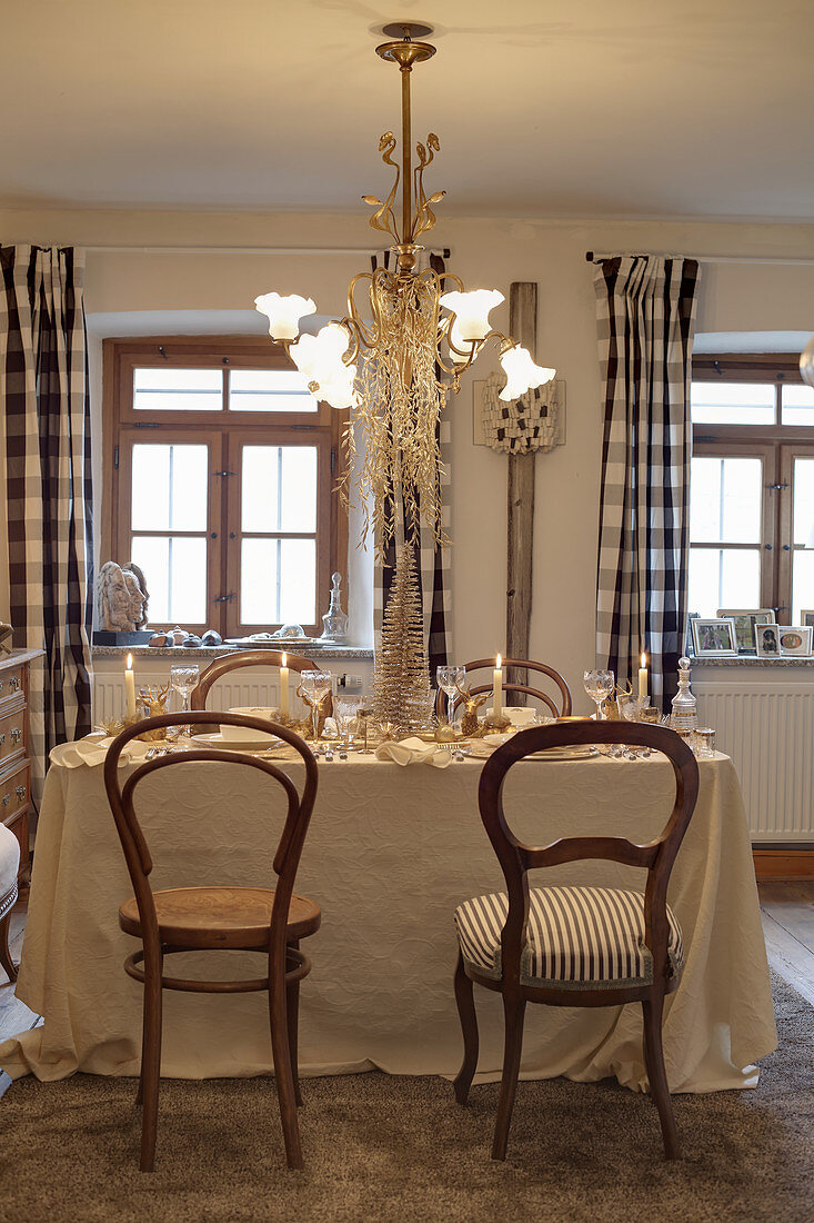 Table set for Christmas in beige and gold below decorated chandelier