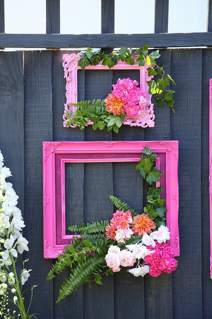 Pinkfarbene Bilderrahmen mit Blumen dekoriert, an Holzwand im Garten
