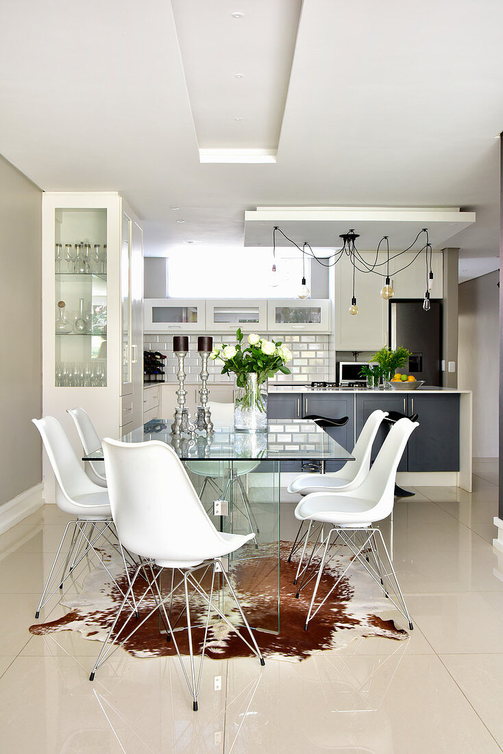 Glass table, classic chairs, cowhide rug and shiny tiled floor in elegant dining area