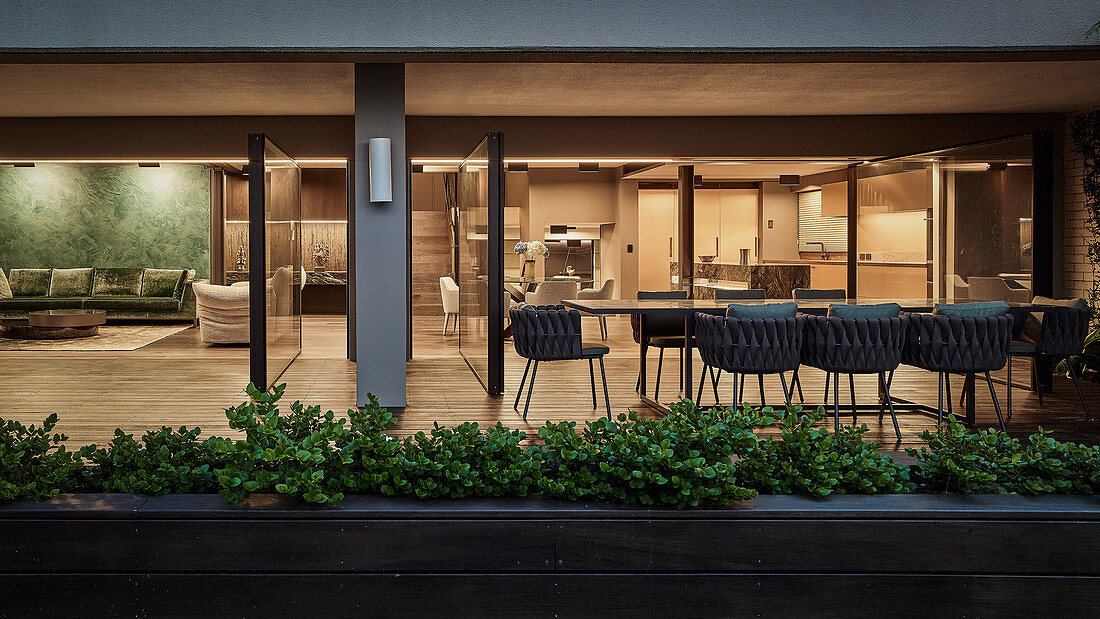 Langer Tisch mit Designer-Outdoor- Sesseln auf der Terrasse, Blick in offenen Wohnraum mit Küche und Lounge