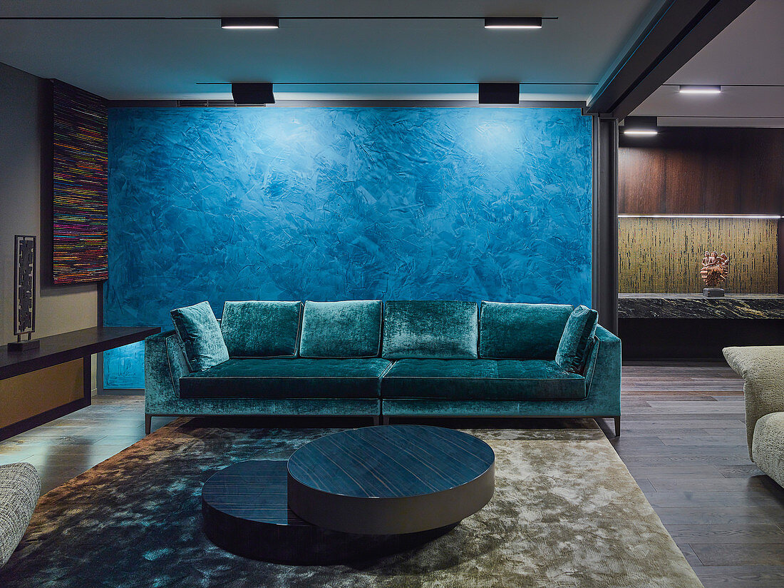 Elegant TV room with designer sofas against blue partition in open-plan interior