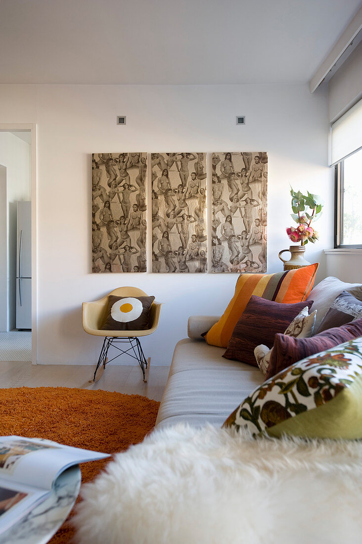 Sofa mit Kissen und Klassikerstuhl unter dreiteiligem Bild im Wohnraum
