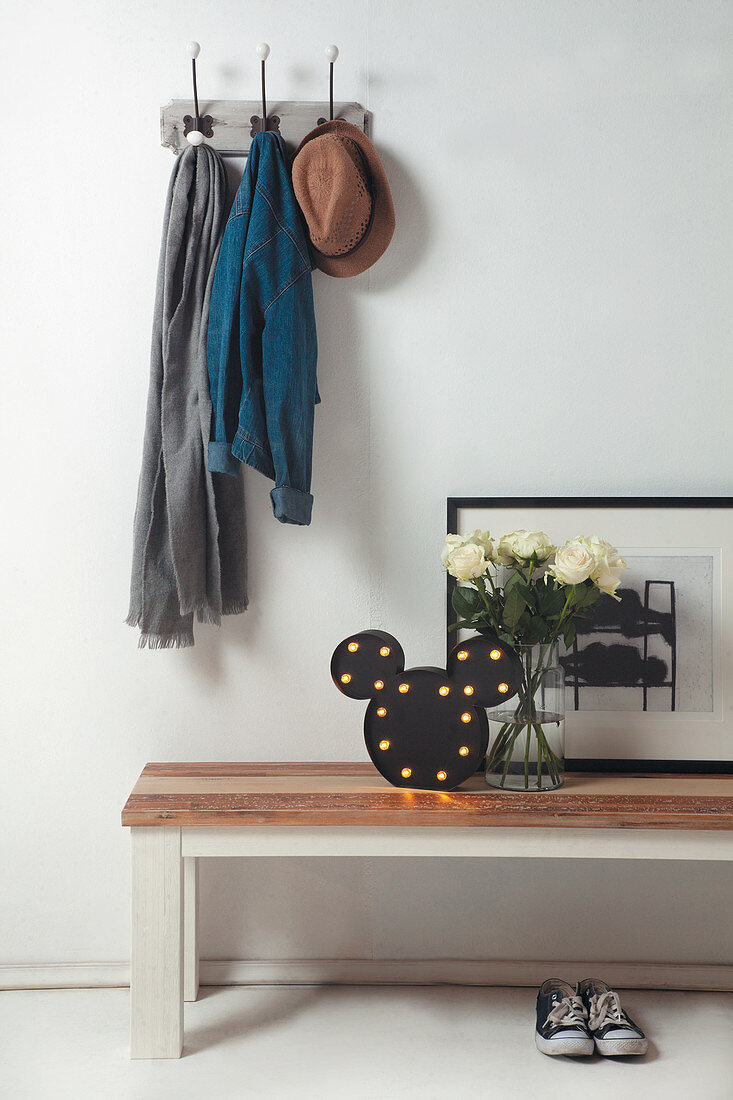 Lamp, roses and picture on wooden bench below coat pegs in hall