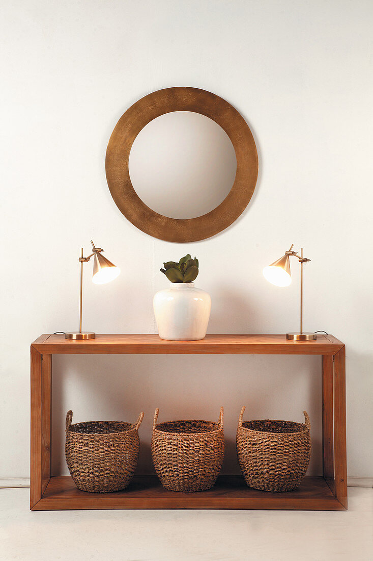 Holzkonsole mit Bambuskörben, Tischleuchten und Vase, darüber runder Wandspiegel