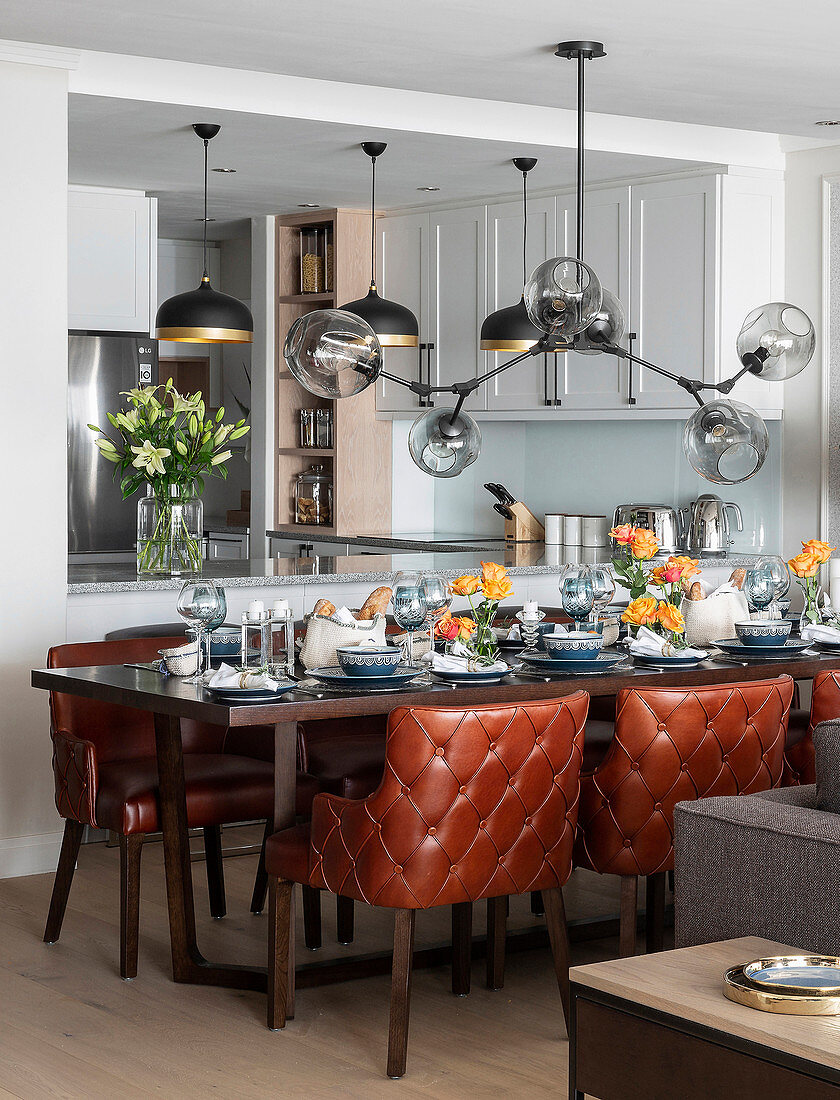 Festively set dining table, custom leather chairs and sculptural light fitting with glass lampshades