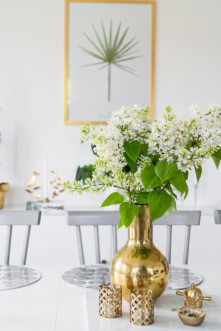 Weiße Fliederblüten in goldener Vase mit goldener Deko auf dem Tisch