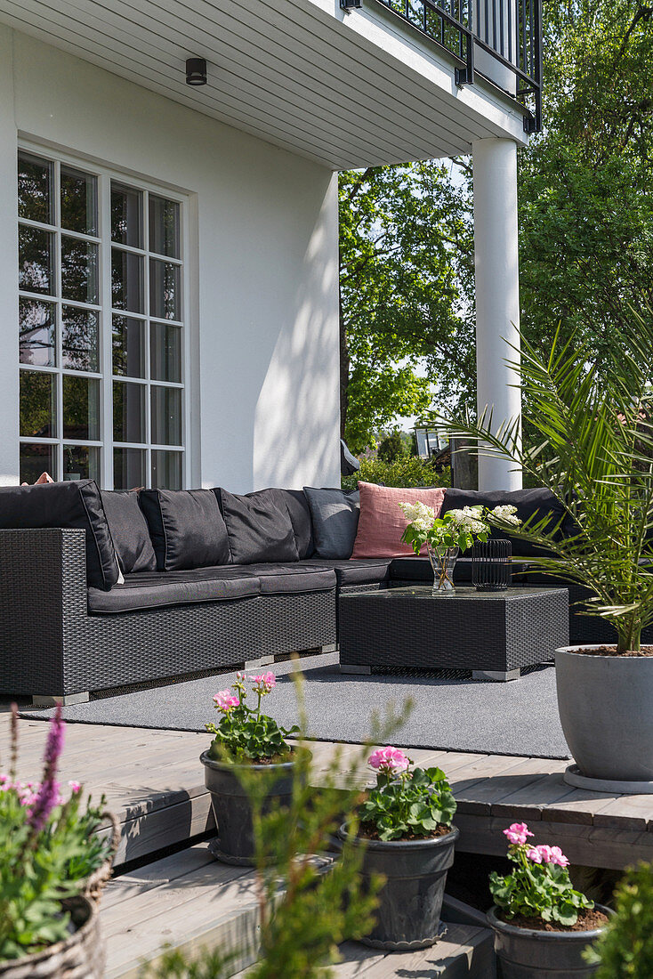 Schwarzes Outdoorsofa auf sommerlicher Terrasse mit Topfpflanzen