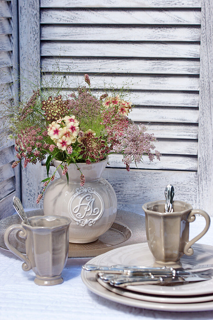 Blumenstrauß mit Wilde-Möhre-Blüten in Vase, davor graues Tischgeschirr