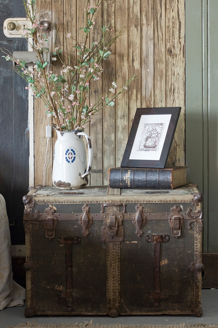 Krugvase mit Blütenzweigen, Buch und Zeichnung auf altem Überseekoffer