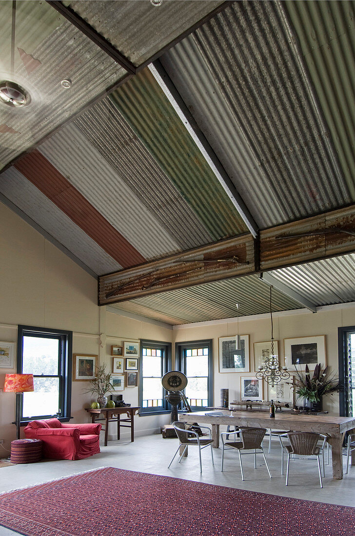 Essbereich mit rustikalem Holztisch, roter Sessel in offenem Wohnraum mit Wellblechdach