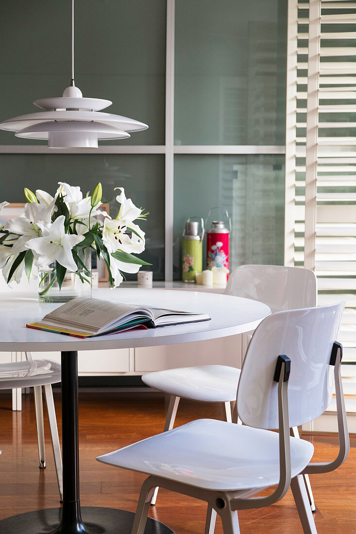 Runder Tisch mit weißen Stühlen, Blumenstrauß und aufgeschlagenes Buch
