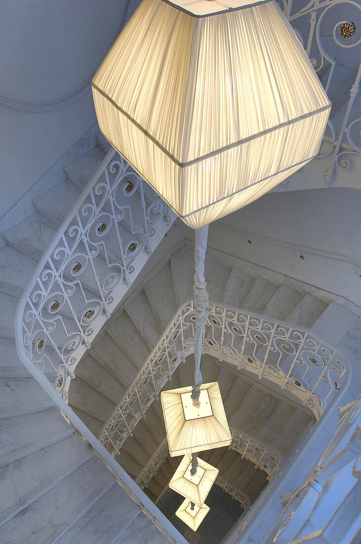 White staircase and wrought-iron balustrade in tall stairwell with vertical string of lights