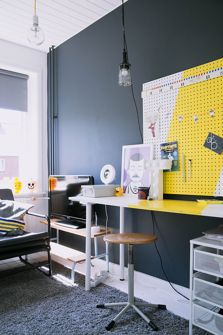 Schreibtisch mit gelb-weißer Pinnwand vor dunkelgrauer Wand in Jugendzimmer