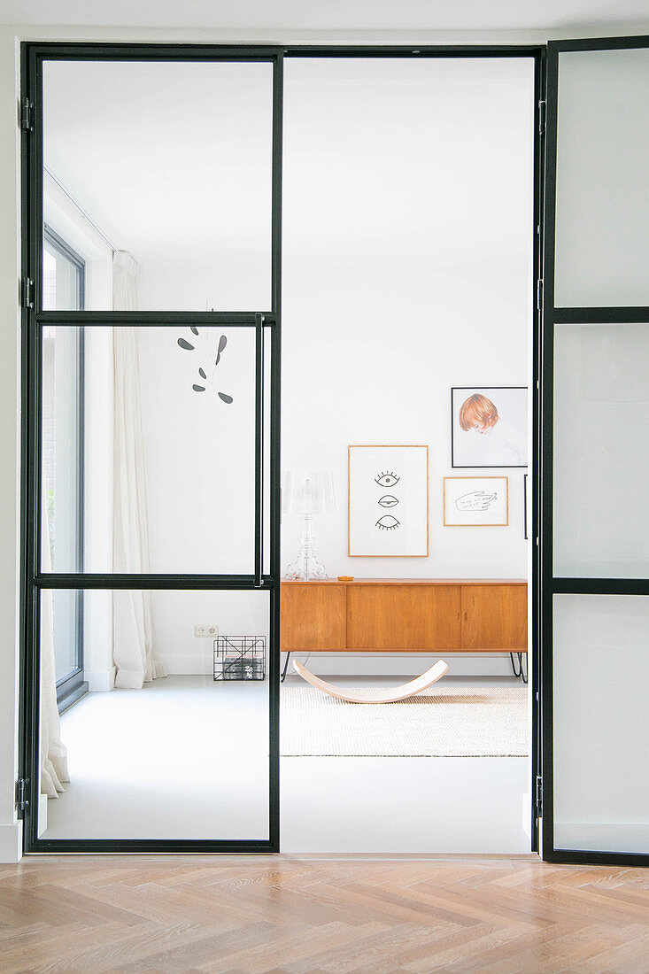 Glass-and-steel door leading to room with baby bouncer and retro sideboard