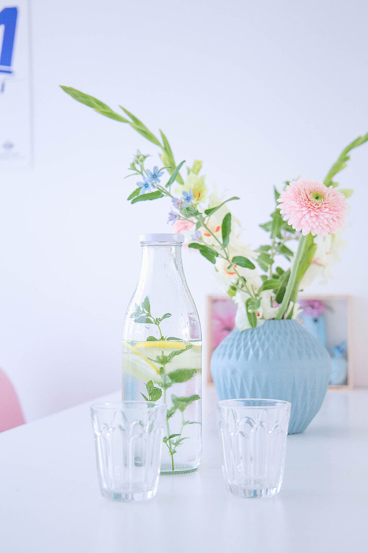 Blumen in hellblauer Vase davor Wasserflasche mit Gläsern auf Esstisch
