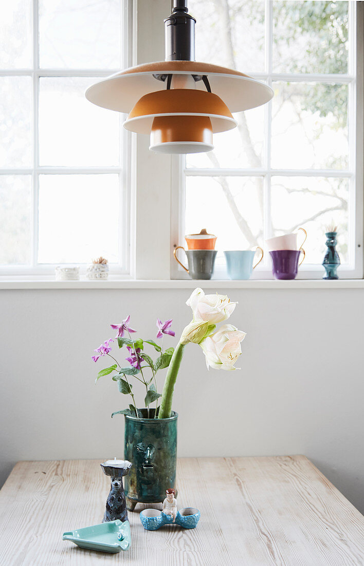 Vase of flowers on table below designer lamp in front of window