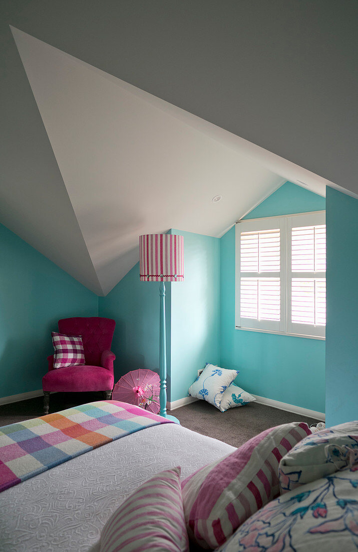 Bett und pinkfarbener Sessel im Zimmer mit hellblauen Wänden