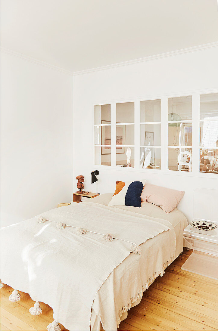 Plaid mit Quasten auf dem Bett vorm Innenfenster im Schlafzimmer