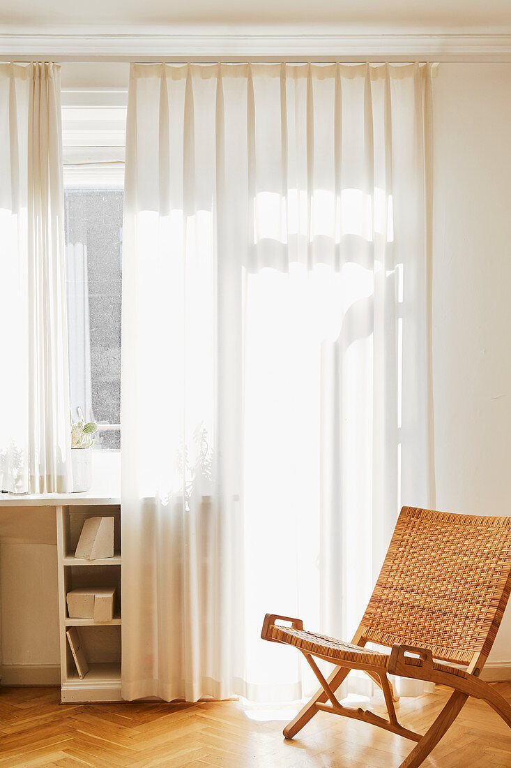 Folding chair with cane backrest and seat in front of window with translucent curtains