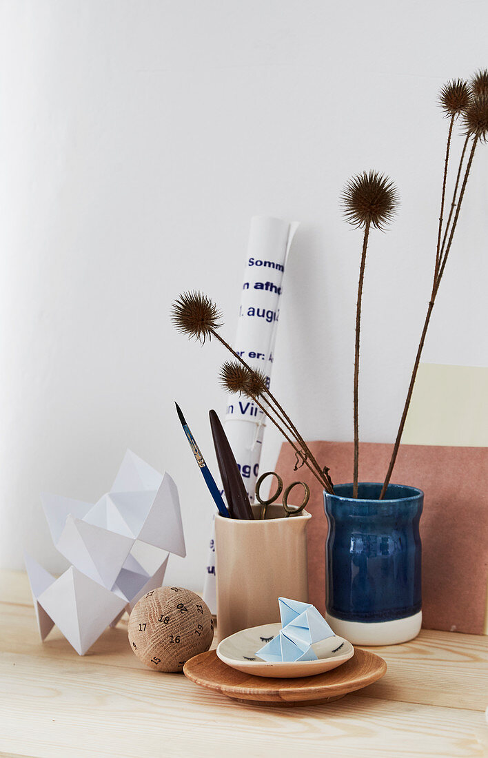 Still-life arrangement of origami, ceramic vessels and dried thistles
