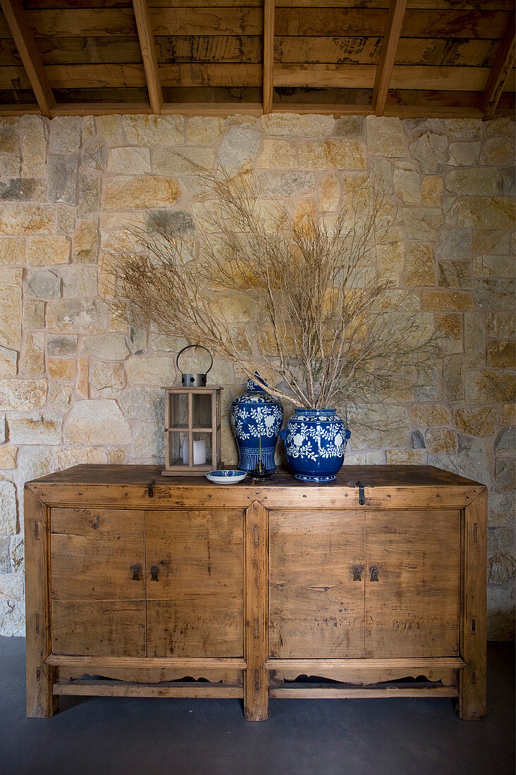 Blau-weiße Vasen und Laterne auf rustikalem Holzschrank vor Natursteinwand