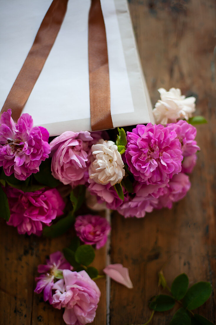 Pinkfarbene Rosen in Papiertüte auf Holztisch
