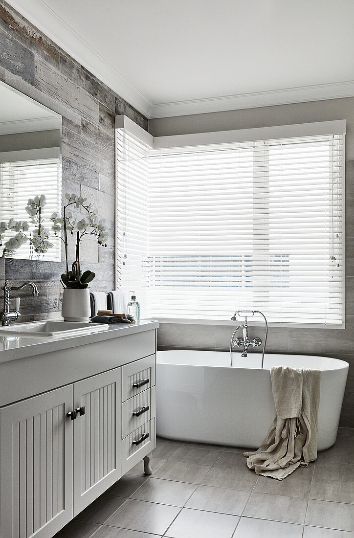 Waschtischmöbel und frei stehende Badewanne im Badezimmer, Fenster mit Jalousie
