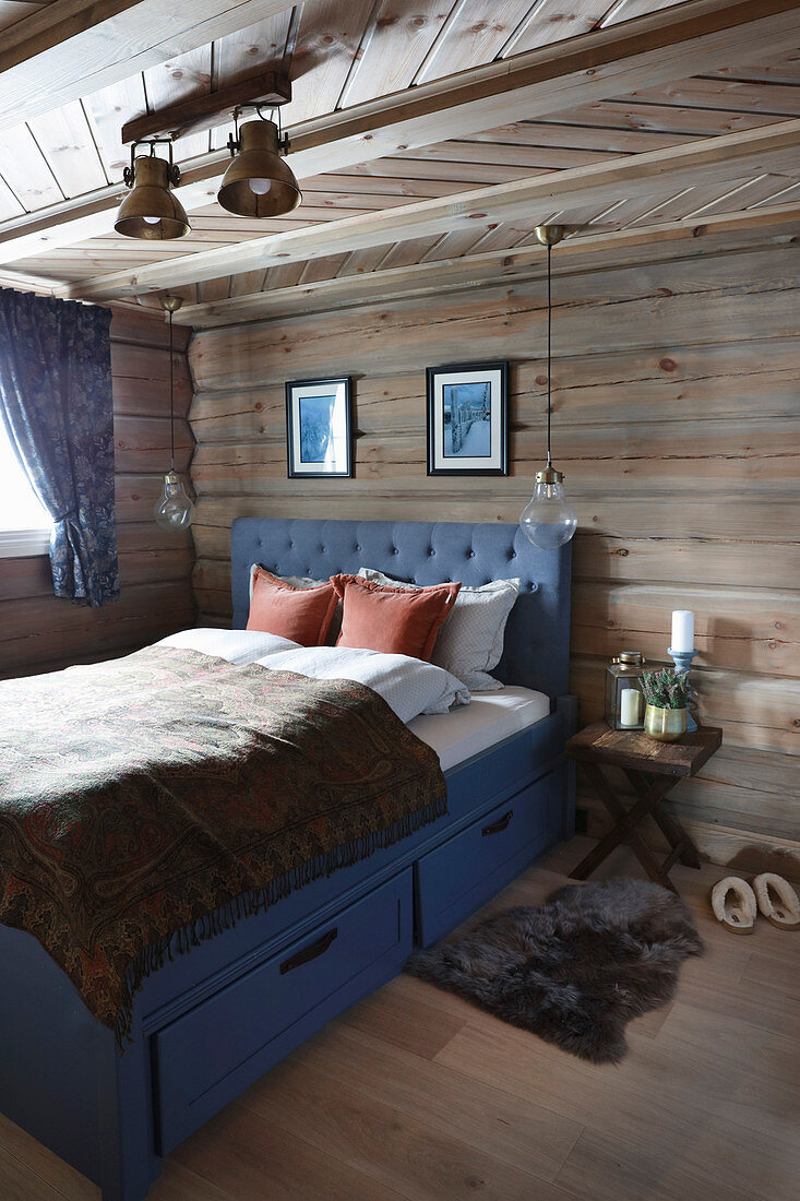 Blue bed with storage drawers and fur rug in log cabin