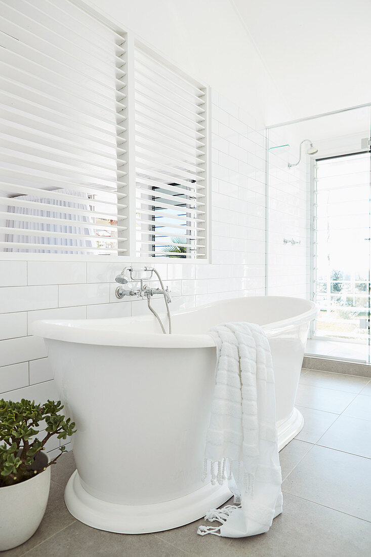 Classic freestanding bathtub in the bathroom in white with louvre windows