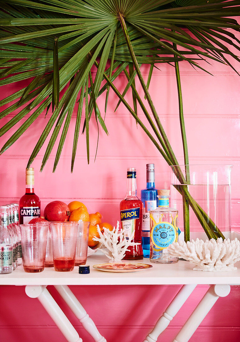 Hausbar auf weißem Tisch vor rosa Wand dekoriert mit Korallen und Palmebwedel
