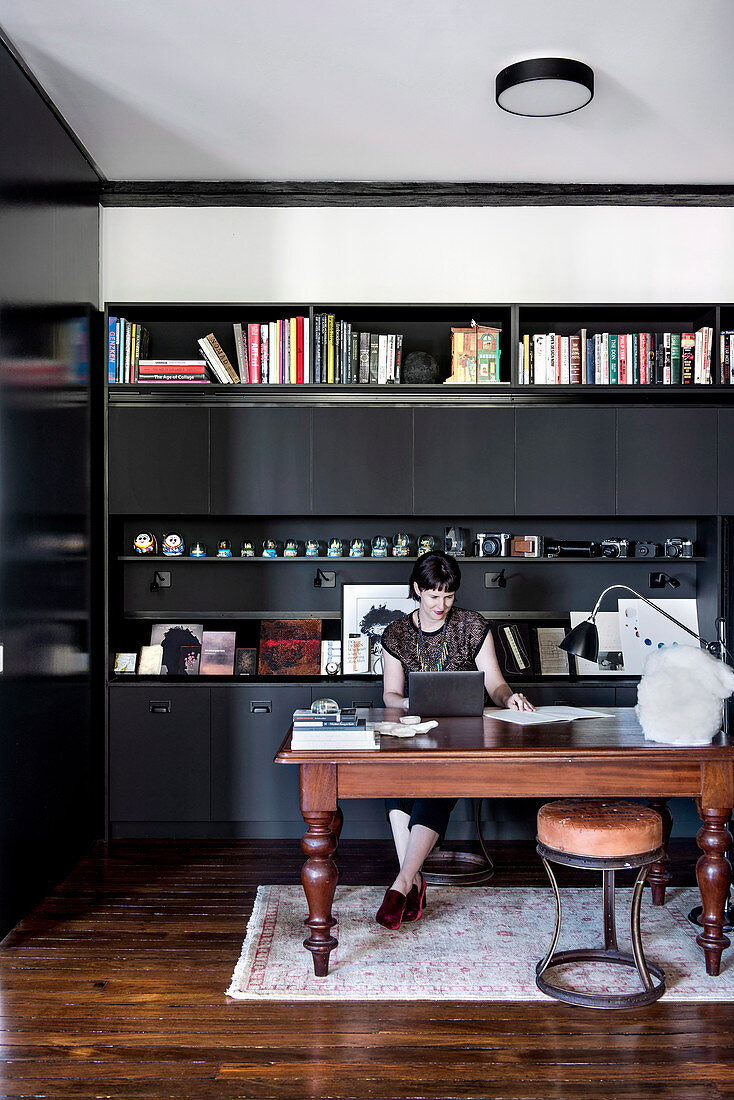 Woman sitting at a wooden table in front of a black wall unit in the office